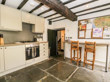 A kitchen with wooden chairs a stove oven and a bulletin board at Duddon Cottage in Broughton-in-Furness
