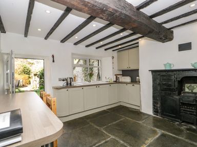 A kitchen with wooden beams on the ceiling cabinets and a black cast iron stove at Duddon Cottage Broughton in Furness