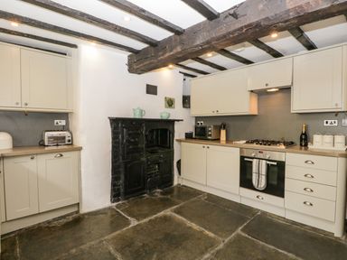 A kitchen with stone floor wooden beams white cabinets and a black cast iron stove at Duddon Cottage Broughton-in-Furness