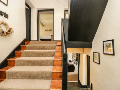 A stairway with carpeted steps and black handrail leading to a room with a bed at Duddon Cottage in Broughton-in-Furness