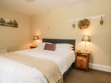 A bedroom with a bed a beige blanket two bedside tables lamps and a wall decoration at Duddon Cottage in Broughton-in-Furness