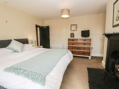 A bedroom with a bed a dresser a small television and a fireplace at Duddon Cottage in Broughton-in-Furness