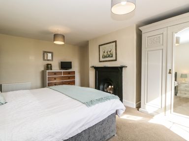 A bedroom with a bed a chest of drawers a fireplace an armoire and two ceiling lights at Duddon Cottage in Broughton-in-Furness