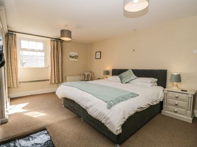 A bedroom with a large bed bedside tables lamps a window and a chair at Duddon Cottage in Broughton-in-Furness