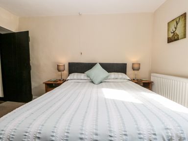 A bedroom with a bed with pillows two bedside tables with lamps a radiator and a painting of a deer at Duddon Cottage in Broughton-in-Furness