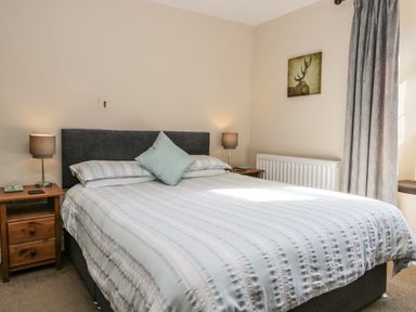 A bedroom with a double bed two bedside tables with lamps a wall painting and curtains at Duddon Cottage in Broughton-in-Furness