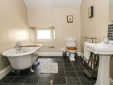 A bathroom with a freestanding clawfoot tub a toilet a pedestal sink a small window and black tiled floor at Duddon Cottage in Broughton-in-Furness