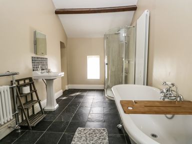 A bathroom with a bathtub, a shower enclosure, a sink, and a wooden shelf at Duddon Cottage in Broughton-in-Furness