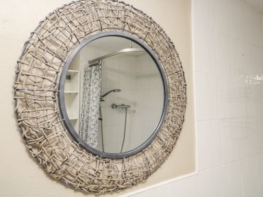 A round mirror with woven frame reflecting a showerhead and curtain in a bathroom at Duddon Cottage in Broughton-in-Furness