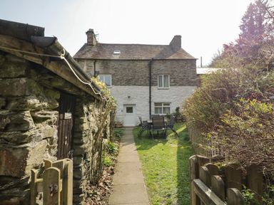 A stone cottage with a white door and windows a pathway leading to the door outdoor table and chairs a wooden fence and garden at Duddon Cottage in Broughton-in-Furness
