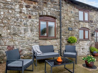 An outdoor patio with black wicker chairs and a table in front of a stone building at The Stables in Llanfair Caereinion near Welshpool