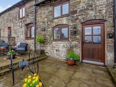 An outdoor stone patio with a wooden door and windows on a stone building at The Stables in Llanfair Caereinion near Welshpool