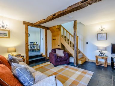 A living room with sofa and armchair near stairs and a doorway leading to a dining area at The Stables in Llanfair Caereinion near Welshpool
