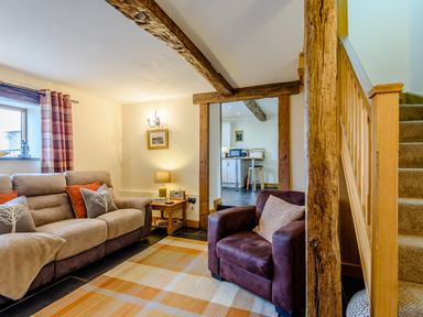 A living room with a sofa, armchair, lamp, side table, and staircase at The Stables in Llanfair Caereinion near Welshpool