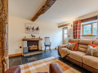 A living room with a sofa pillows fireplace and wooden beams at The Stables in Llanfair Caereinion near Welshpool