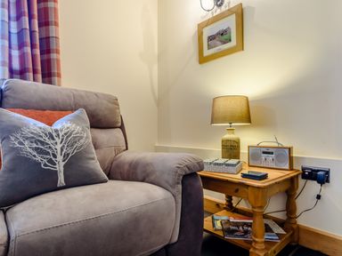 A corner of a living room with a gray armchair next to a wooden side table with a lamp radio and magazines at The Stables in Llanfair Caereinion near Welshpool