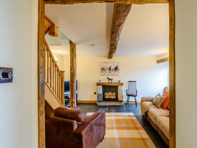 A living room with wooden beams a fireplace two armchairs a sofa and a checkered rug at The Stables in Llanfair Caereinion near Welshpool