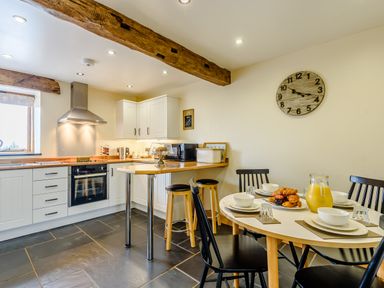 A kitchen with a wooden countertop and white cabinets and a dining table set with bowls and a jug of juice at The Stables in Llanfair Caereinion near Welshpool