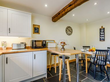 A kitchen with wooden countertops white cabinets stools a microwave toaster clock and a dining table with chairs at The Stables in Llanfair Caereinion near Welshpool