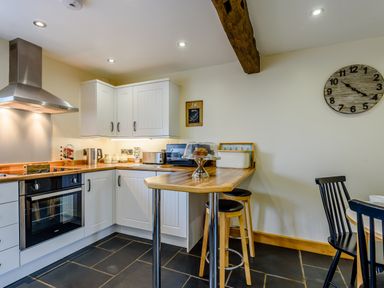 A kitchen with white cabinets a wooden countertop stools a clock on the wall and kitchen appliances at The Stables in Llanfair Caereinion near Welshpool