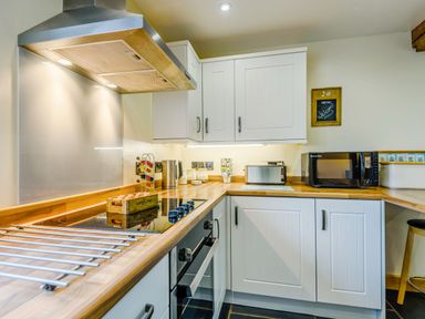 A kitchen with white cabinets wooden countertop stovetop oven microwave and toaster at The Stables in Llanfair Caereinion near Welshpool