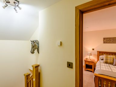 A hallway with wooden staircase and horse head sculpture near a bedroom with wooden bed and bedside table at The Stables in Llanfair Caereinion near Welshpool