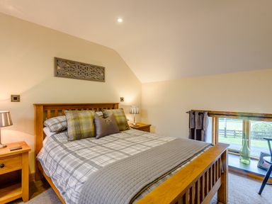 A bedroom with a wooden double bed plaid bedding bedside tables lamps and a window with a view at The Stables in Llanfair Caereinion near Welshpool