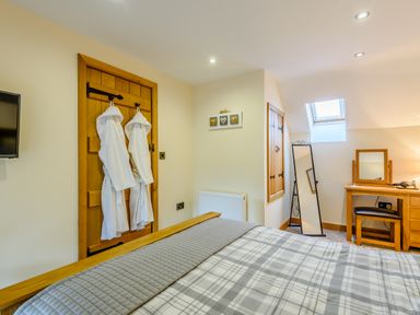 A bedroom with a bed a dressing table mirror and robes hanging on a wooden door at The Stables Llanfair Caereinion near Welshpool