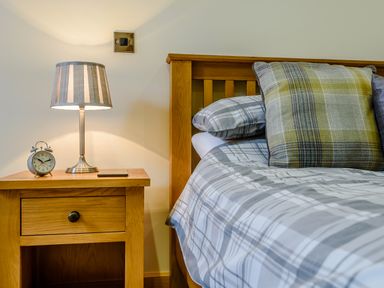 A bedroom with a wooden bed and bedside table with a striped lamp and clock at The Stables in Llanfair Caereinion near Welshpool