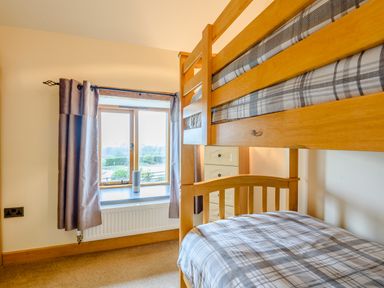 A bedroom with wooden bunk beds and a window with curtains at The Stables in Llanfair Caereinion near Welshpool