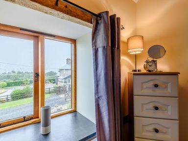 A window with curtains next to a chest of drawers with a lamp clock and mirror at The Stables in Llanfair Caereinion near Welshpool