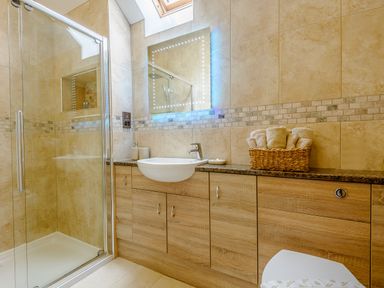 A bathroom with a glass shower enclosure a sink with countertop cabinets and a basket of towels on the counter at The Stables in Llanfair Caereinion near Welshpool