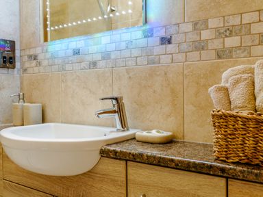 A bathroom sink with a chrome faucet soap dispenser and a basket of rolled towels at The Stables in Llanfair Caereinion near Welshpool
