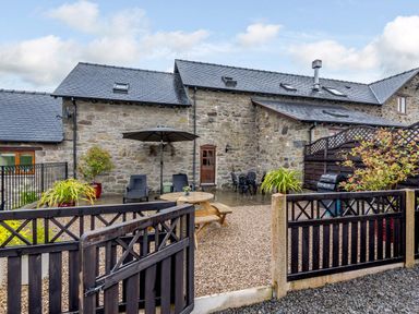 A stone house with a patio garden enclosed by a black wooden fence with outdoor furniture and plants at The Stables in Llanfair Caereinion near Welshpool
