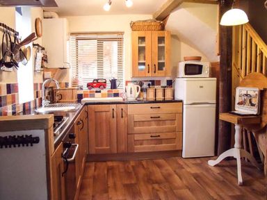 A kitchen with wooden cabinets a refrigerator microwave and a small table at Groom Cottage in Poughill near Bude