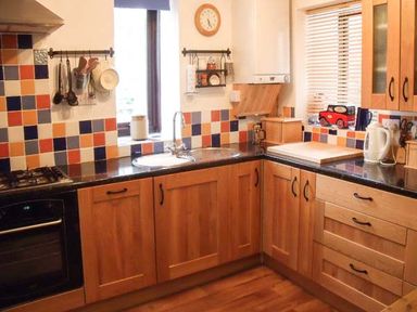 A kitchen with wooden cabinets tiled backsplash black countertops a sink and various kitchen utensils at Groom Cottage in Poughill near Bude