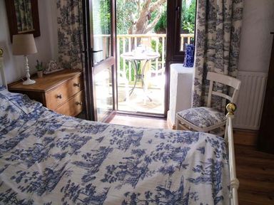 A bedroom with a bed a wooden dresser a chair and open doors leading to a balcony at Groom Cottage in Poughill near Bude