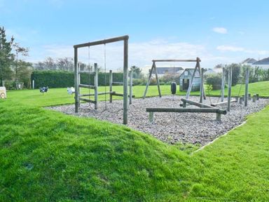 An outdoor children's playground with swings and climbing structures on grass at Groom Cottage in Poughill near Bude