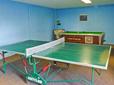 A game room with a green ping pong table and a pool table with a chair against a blue wall at Groom Cottage in Poughill near Bude
