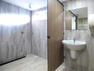 A tiled bathroom with a wall-mounted sink a mirror a wooden door and a walk-in shower area at Groom Cottage in Poughill near Bude