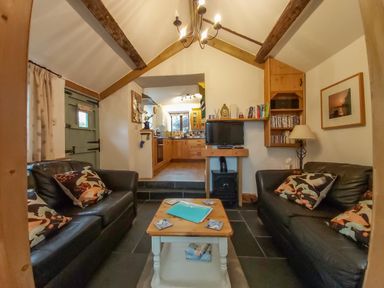 A living room with two black sofas a wooden coffee table a television and a view into a kitchen at Groom Cottage in Poughill near Bude