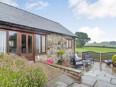An outdoor patio with chairs and table next to a stone building with wooden doors and windows at The Granary in Llanfair Caereinion near Welshpool