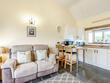A living room with a sofa and cushions next to a kitchen with stools and cabinets at The Granary in Llanfair Caereinion near Welshpool