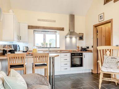 A kitchen with wooden chairs and table a fruit jug an oven and a window at The Granary in Llanfair Caereinion near Welshpool