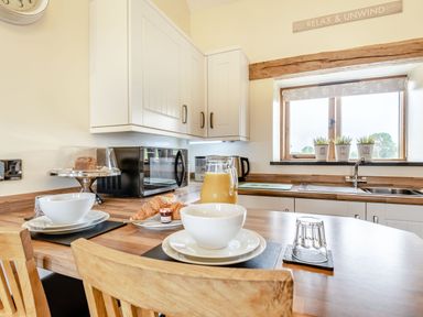 A kitchen table with bowls croissants and juice next to a microwave and a window with plants at The Granary in Llanfair Caereinion near Welshpool