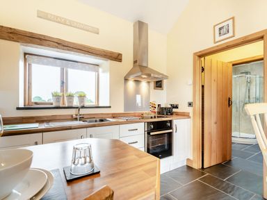 A kitchen with wooden countertops white cabinets and a stainless steel oven next to a wooden door leading to a bathroom at The Granary in Llanfair Caereinion near Welshpool
