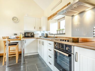 A kitchen with white cabinets wooden countertop oven stovetop a small wooden breakfast bar and a window at The Granary in Llanfair Caereinion near Welshpool