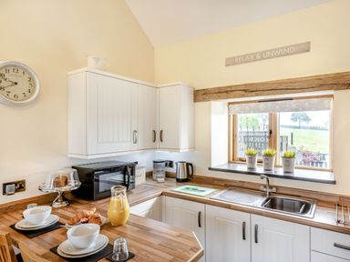 A kitchen with white cabinets a wooden countertop a window with plants and kitchenware a microwave and breakfast items at The Granary in Llanfair Caereinion near Welshpool