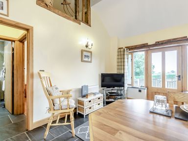 A dining area with a wooden table and chair a television on a stand and patio doors with a view outside at The Granary in Llanfair Caereinion near Welshpool