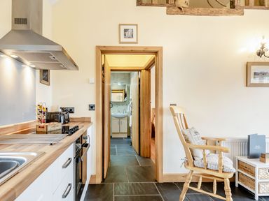 A kitchen with a stove and sink next to a wooden rocking chair and a doorway leading to a bathroom at The Granary in Llanfair Caereinion near Welshpool